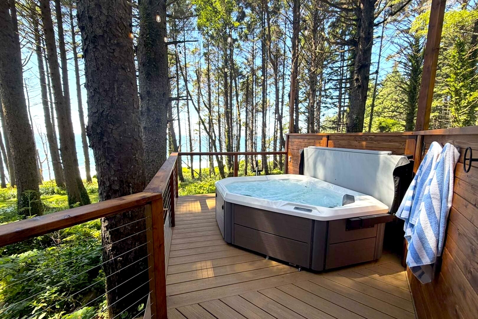 Hot tub on a forested deck with ocean glimpse through the trees