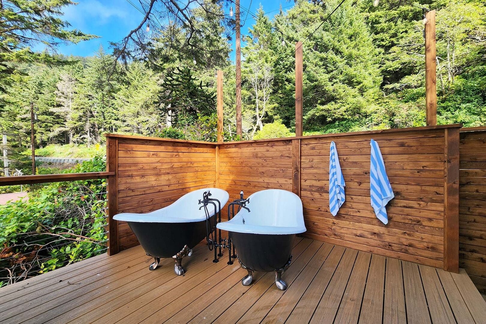 Outdoor clawfoot soaking tubs on a private deck surrounded by forest